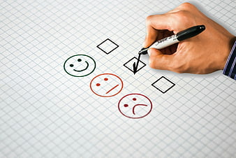 Hand checking satisfaction survey with smiley faces on grid paper
