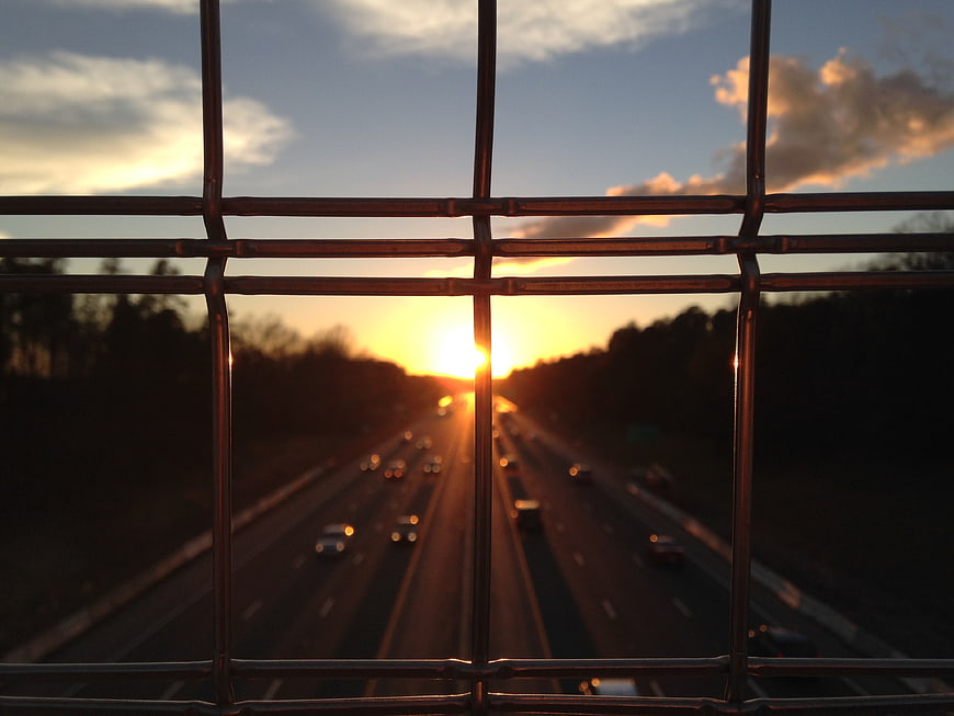 Sunset View Through Metal Fence on Busy Highway