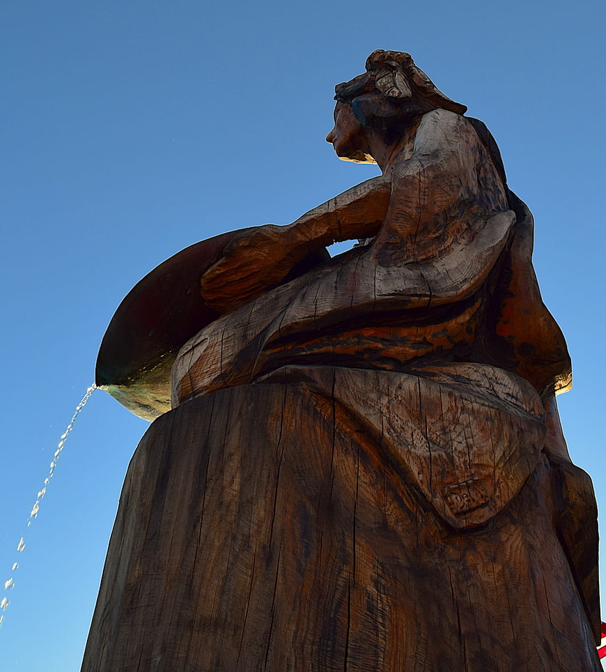 Low angle view of wooden fountain sculpture against blue sky