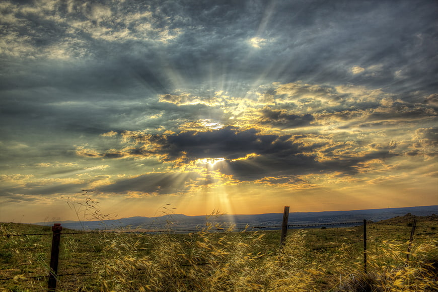 Dramatic sunset with sun rays breaking through clouds over a grassy field