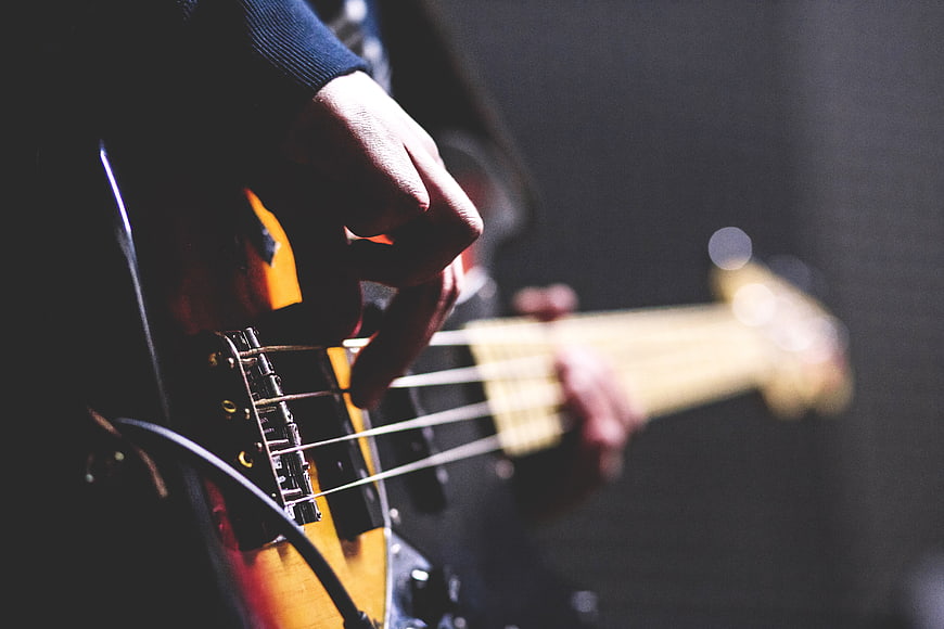 Close-up of hands playing electric bass guitar on stage