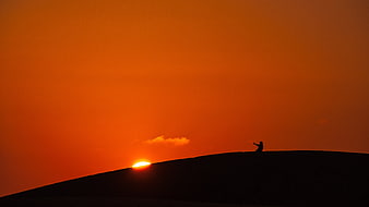 Silhouette of person on hilltop during vibrant orange sunset