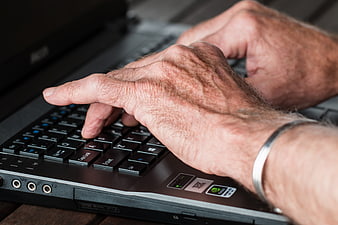 Close-up of elderly hands typing on a laptop keyboard