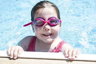 Happy young girl wearing pink swimming goggles in a blue pool