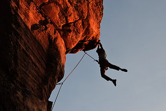 Rock climber hanging from red cliff against blue sky