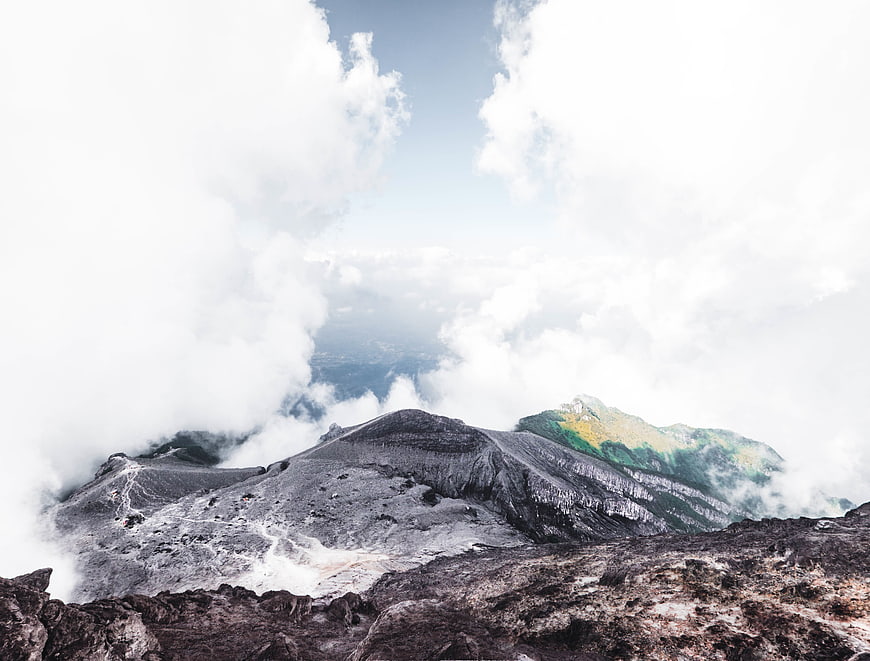 Volcanic crater rim with clouds and distant green mountain