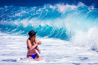 Woman in Blue Bikini and Hat Kneeling in Ocean Waves