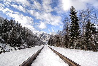 Snow-covered railway tracks leading to mountains in winter