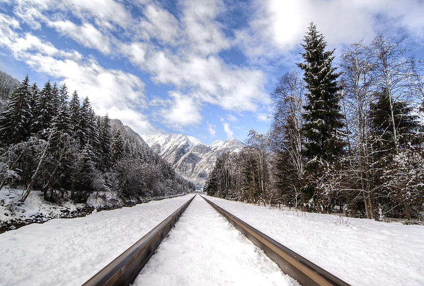 Snow-covered railway tracks leading to mountains in winter