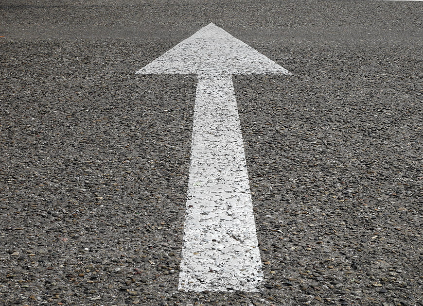 White directional arrow painted on gray asphalt road surface