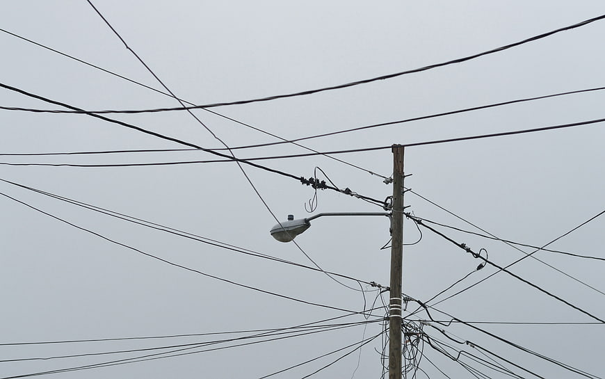 Tangled utility wires and street lamp against gray sky