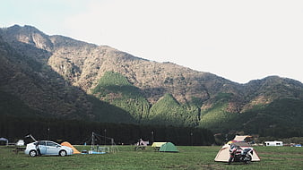 Camping site with tents, car, and motorcycle in mountain valley