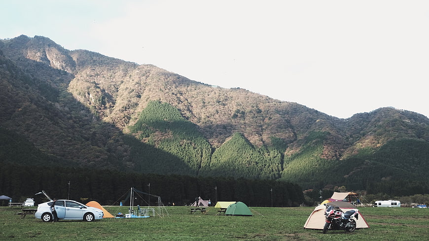 Camping site with tents, car, and motorcycle in mountain valley