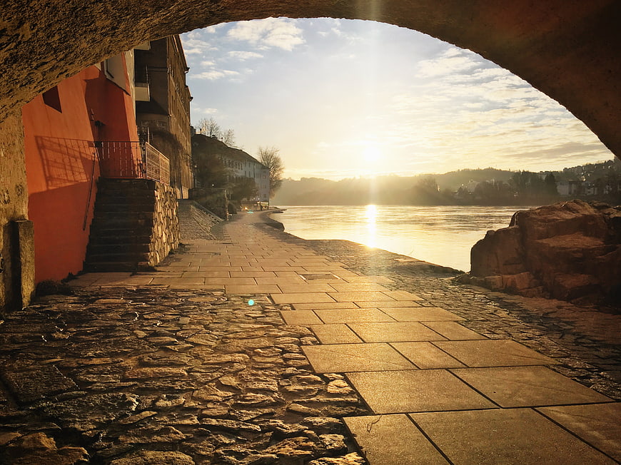 Sunset View Through Stone Arch Over River Walkway