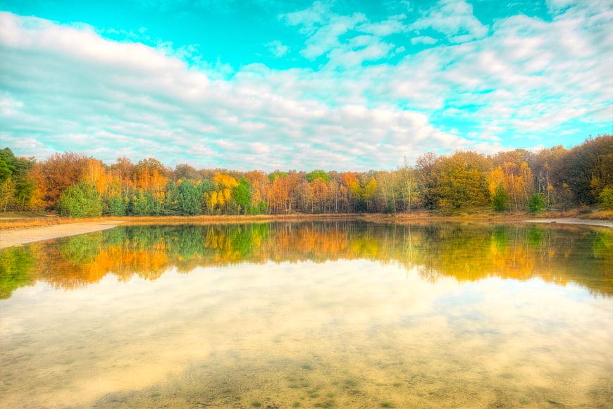 Serene autumn lake with colorful forest reflection and blue sky