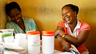 Two smiling women laughing with medical supplies on a table