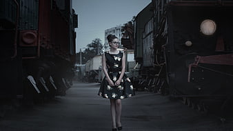 Young woman in floral dress standing between vintage trains at dusk