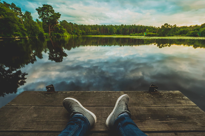 First Person View of Feet Relaxing on Wooden Dock by Lake