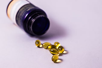 Spilled yellow vitamin capsules from blue bottle on white background