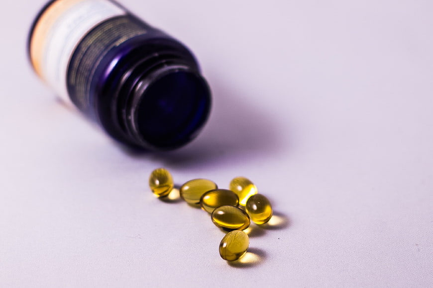 Spilled yellow vitamin capsules from blue bottle on white background