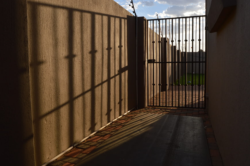Sunlit alleyway with metal gate and dramatic shadows