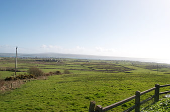 Scenic green countryside landscape with wooden fence and distant ocean view