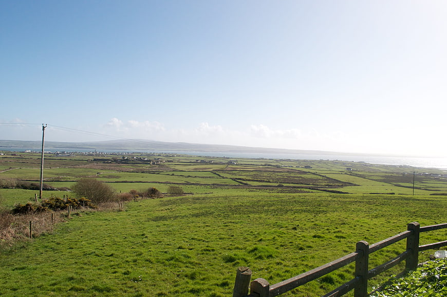 Scenic green countryside landscape with wooden fence and distant ocean view
