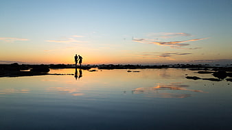 Silhouette of Couple Walking on Beach at Sunset with Reflection