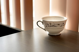 White ceramic teacup on wooden table with soft window light