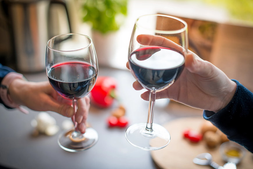 Two Hands Toasting with Red Wine Glasses in Kitchen