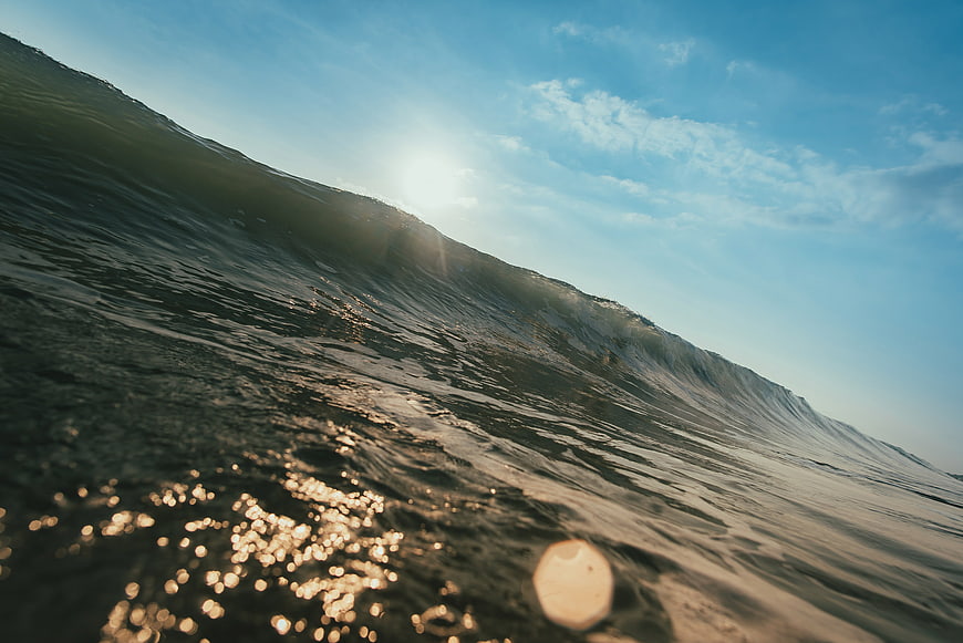 Dramatic Ocean Wave Crest With Sun Flare And Sparkling Water Surface