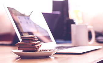 Stack of Biscuits and Laptop on Wooden Desk