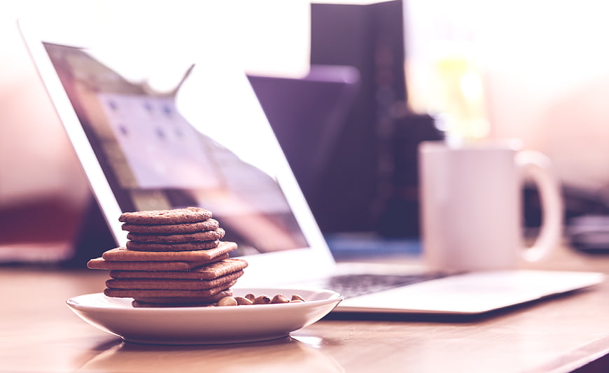 Stack of Biscuits and Laptop on Wooden Desk