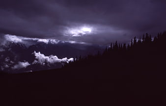 Dramatic dark storm clouds over silhouetted mountain forest