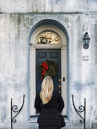 Woman standing before a blue door with a Christmas wreath