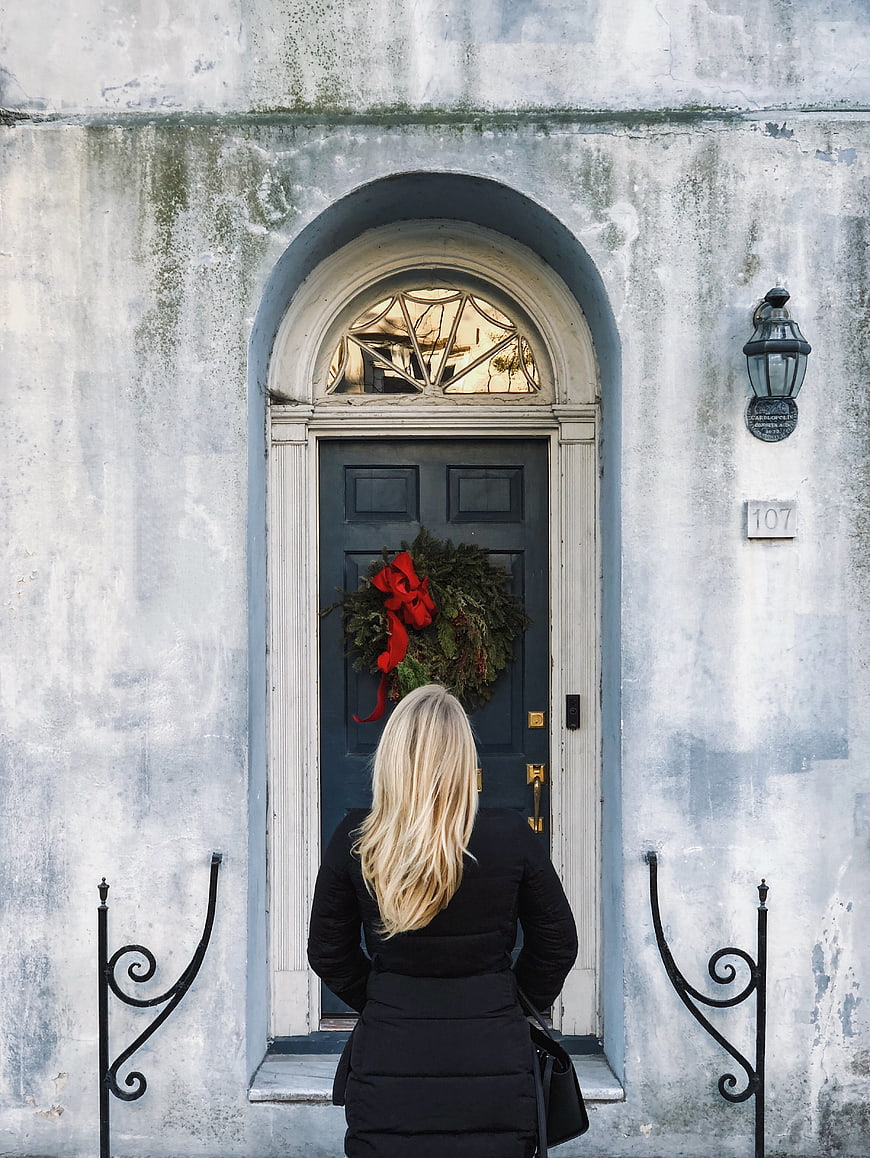 Woman standing before a blue door with a Christmas wreath