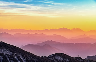 Layered mountain ridges at sunset with colorful sky and hazy atmosphere