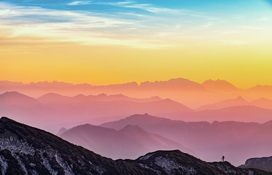 Layered mountain ridges at sunset with colorful sky and hazy atmosphere