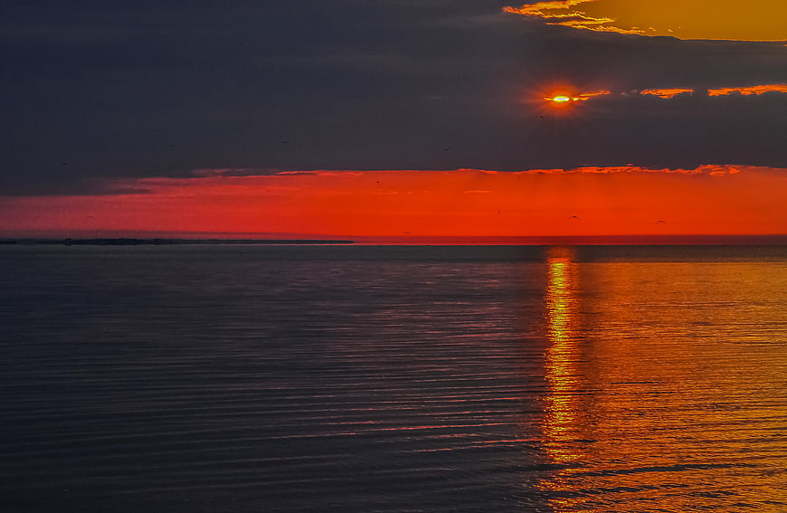 Vibrant Orange Sunset Over Calm Ocean with Clouds