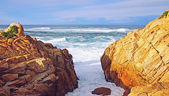 Golden rocky coastline with crashing ocean waves and blue sky
