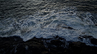 Dark ocean waves crashing on rocks aerial view