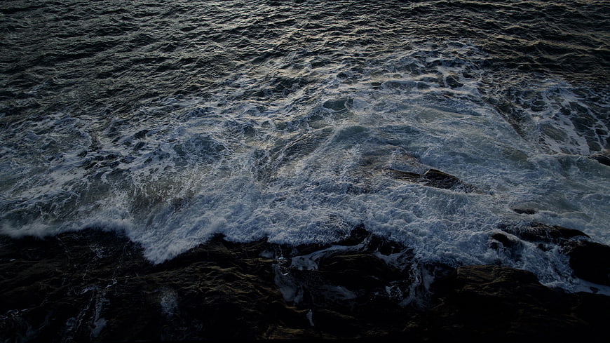 Dark ocean waves crashing on rocks aerial view