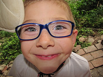 Close-up portrait of a smiling young boy wearing blue glasses