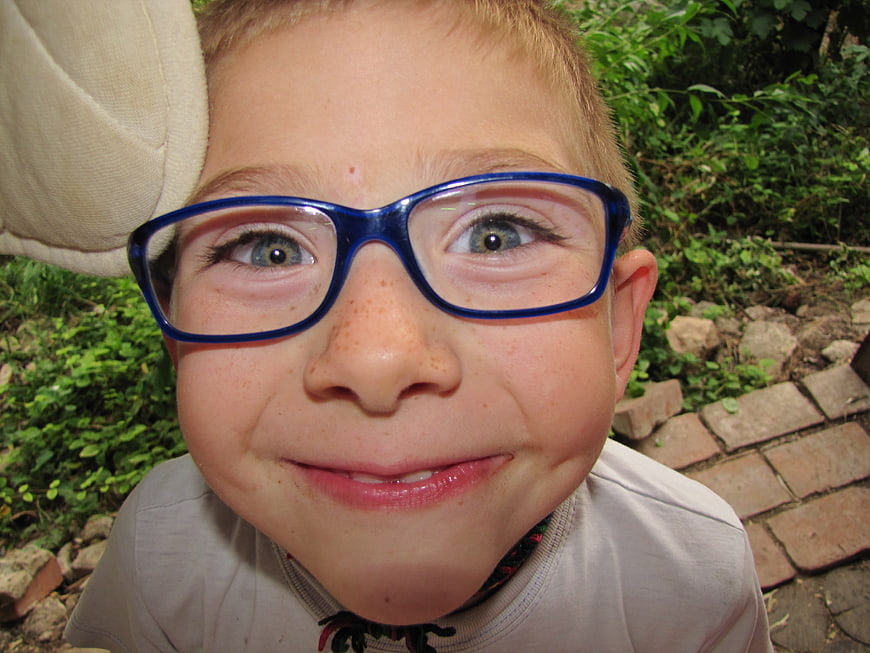 Close-up portrait of a smiling young boy wearing blue glasses