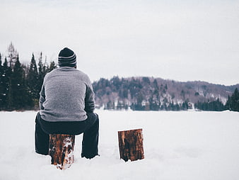 Man Sitting Alone on Log in Snowy Winter Landscape