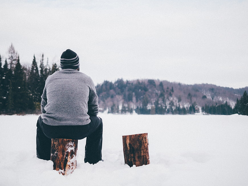 Man Sitting Alone on Log in Snowy Winter Landscape