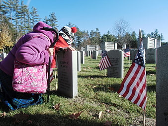 Senior woman visiting veteran grave with American flag in cemetery