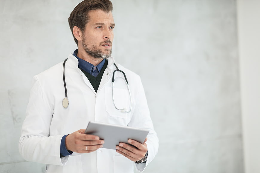 Male Doctor Holding Tablet with Stethoscope Around Neck