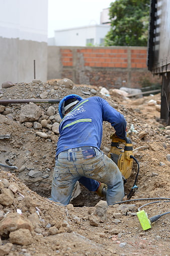 Construction worker using jackhammer in dirt excavation site