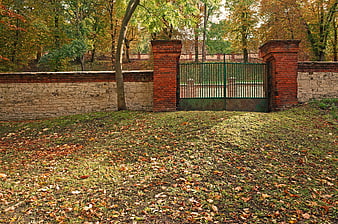 Autumn park entrance with brick wall and green metal gate